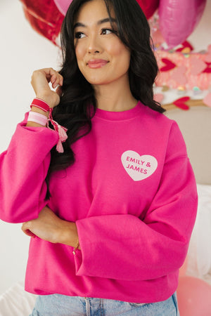 A woman shows off her bright pink sweatshirt personalized with "Emily & James" in a heart.