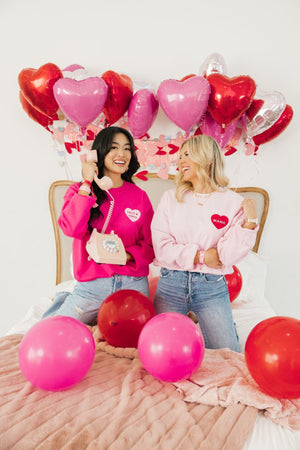 Two women laugh together wearing their pink customized sweatshirts for Valentine's Day