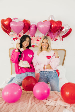 Two women laugh together wearing their pink customized sweatshirts for Valentine's Day