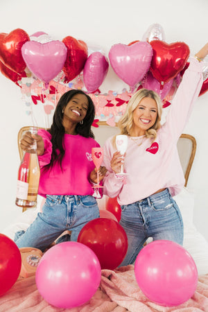 Two women laugh together wearing their pink customized sweatshirts for Valentine's Day