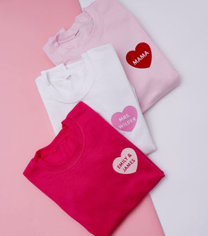 Sweatshirts are laid out to show their customized text inside a heart.