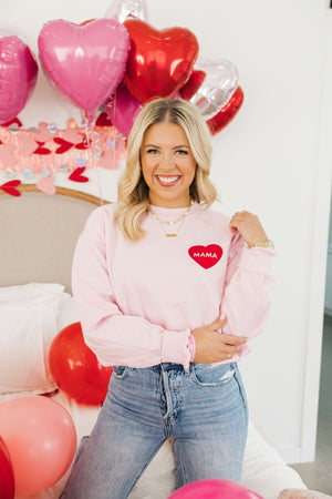 A woman wears a pink sweatshirt decorated with a red heart that reads "Mama"