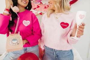 Two women laugh together wearing their pink customized sweatshirts for Valentine's Day