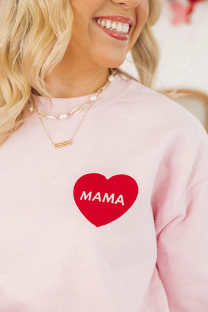 A woman wears a pink sweatshirt decorated with a red heart that reads "Mama"