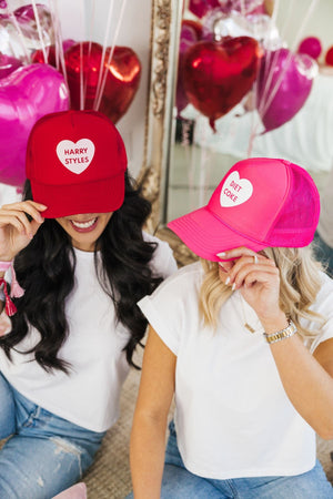 Two women sit showing off their pink and red customized Valentine's Day Hats