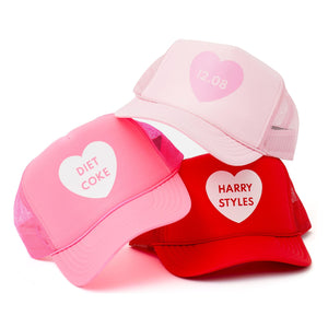 Trucker hats are stacked to show a heart design with customized text inside