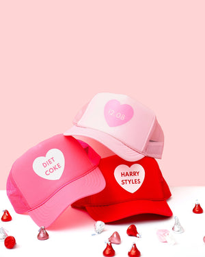 Trucker hats are stacked to show a heart design with customized text inside