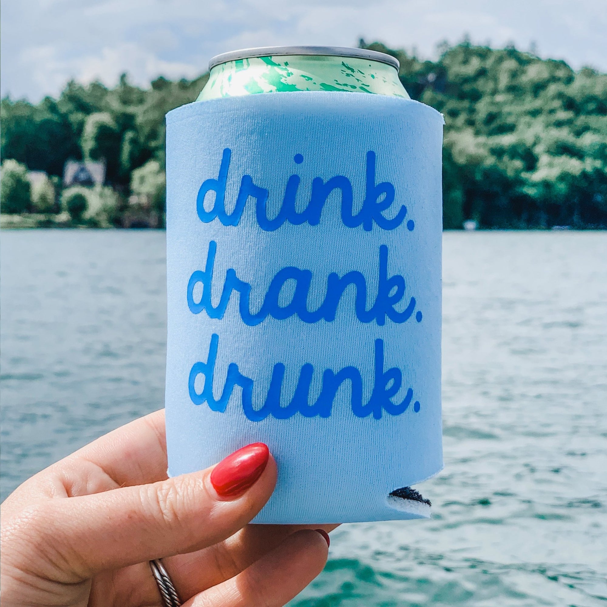 A blue cooler is held up by a woman in a swimsuit and reads "drink drank drunk" in a dark blue font.