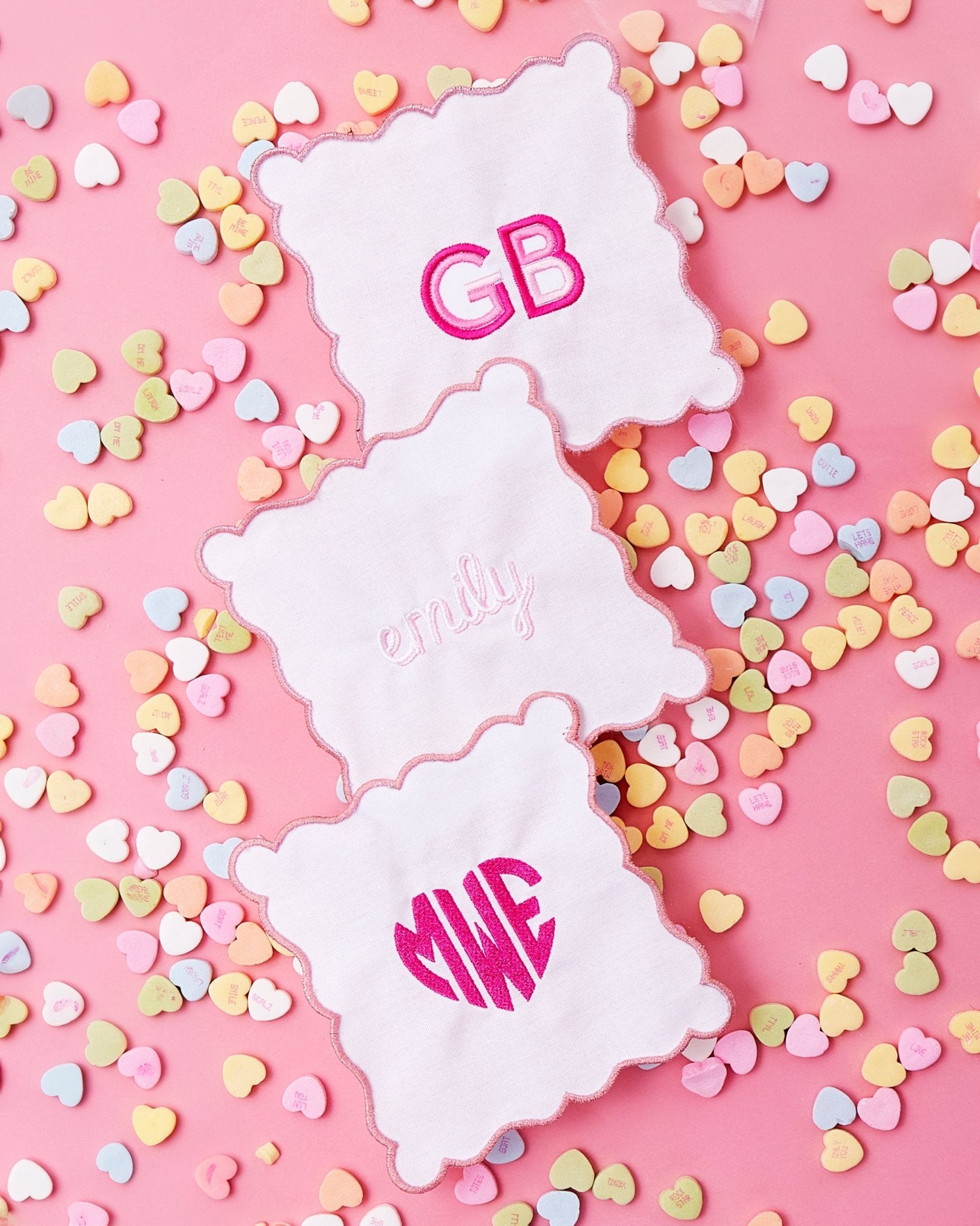 A pink scalloped cocktail napkin is customized with a pink heart monogram