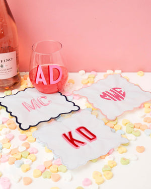 A set of monogrammed cocktail napkins is set up with a bottle of wine and a wine glass