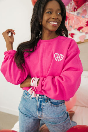 A woman smiles wearing a bright pink sweatshirt embellished with her monogram in a heart