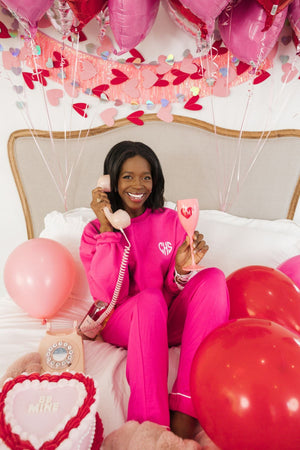 A woman smiles wearing a bright pink sweatshirt embellished with her monogram in a heart