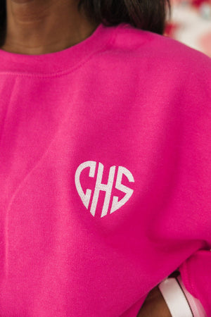 A white monogram is embroidered onto a bright pink sweatshirt in the shape of a heart.