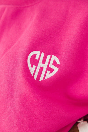 A white monogram is embroidered onto a bright pink sweatshirt in the shape of a heart.