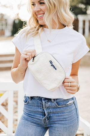 A woman in a white sweatshirt holds her phone which is in a case with a gold foil monogram