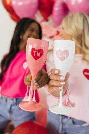 Two girls cheers champagne flutes with hearts to celebrate Valentine's