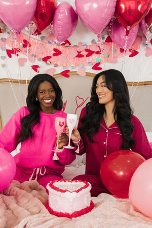 Two girls cheers champagne flutes with hearts to celebrate Valentine's