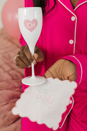 A woman holds up a white champagne flute with a monogrammed heart