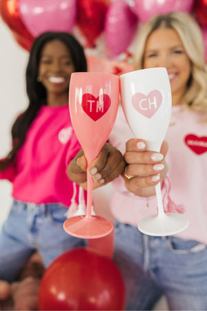 Two girls cheers champagne flutes with hearts to celebrate Valentine's