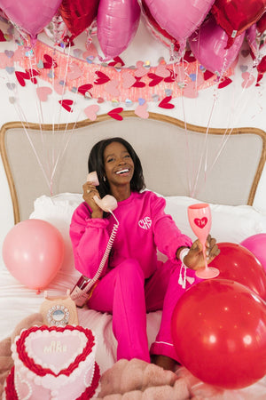 A woman holds up a pink champagne flute with a monogrammed heart