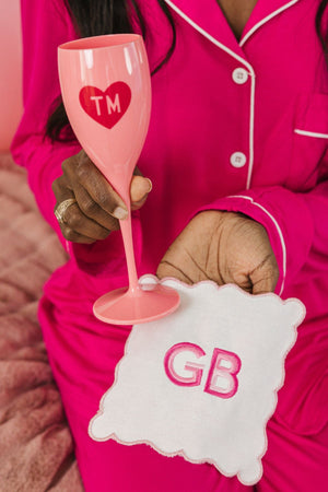 A woman holds up a pink champagne flute with a monogrammed heart