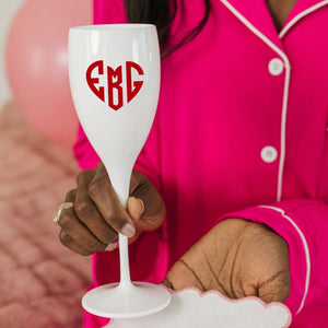 A woman holds up a white champagne flute with a monogrammed heart