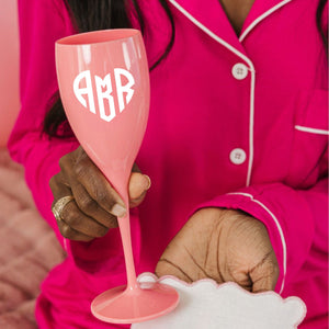 A woman holds up a pink champagne flute with a monogrammed heart