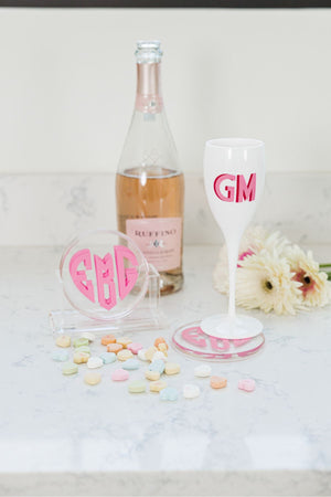 A set of coasters sits next to a bottle of wine and a champagne flute which displays the custom heart monogram