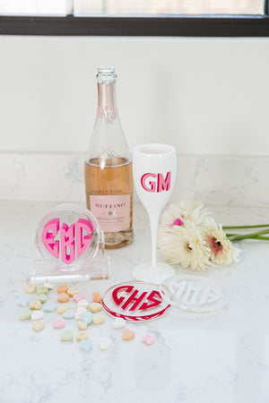 A set of coasters sits next to a bottle of wine and a champagne flute which displays the custom heart monogram