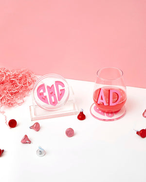 A set of coasters with a heart monogram sits under a wine glass