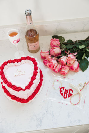 A personalized acrylic tray sits on a countertop next to a cake, flowers and some wine