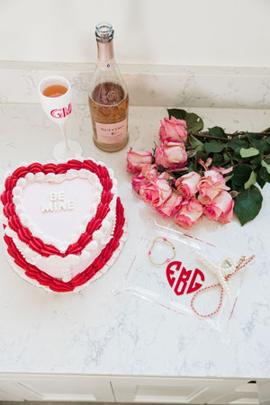 A personalized acrylic tray sits on a countertop next to a cake, flowers and some wine